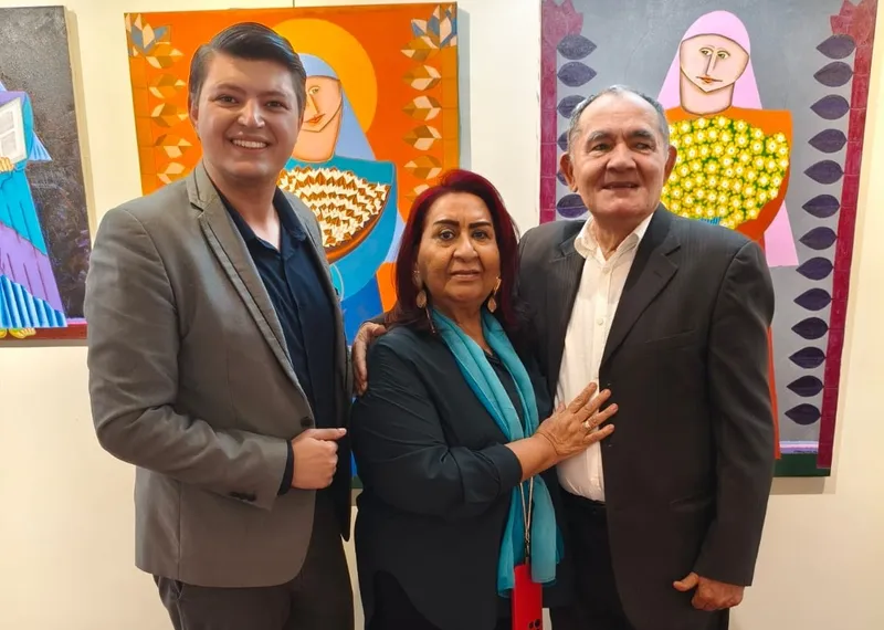 Três pessoas posam em frente a pinturas coloridas na exposição Arte no Quadrado