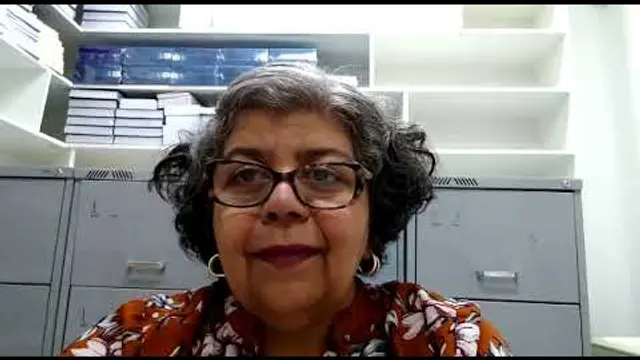 Roseli fala para a câmera em uma sala com estantes e arquivos
